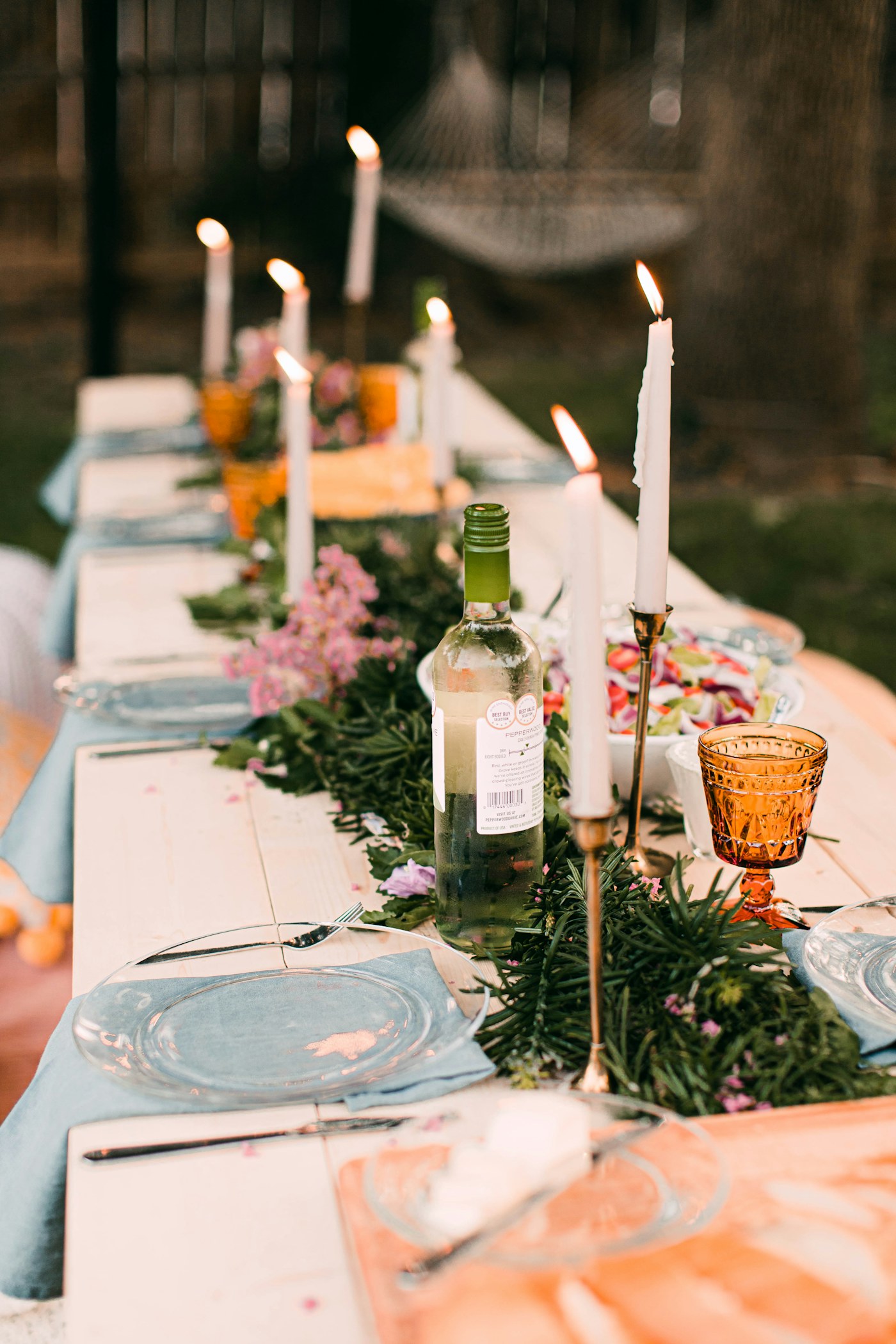 Mesa larga al aire libre con velas, flores y vajilla para una celebración